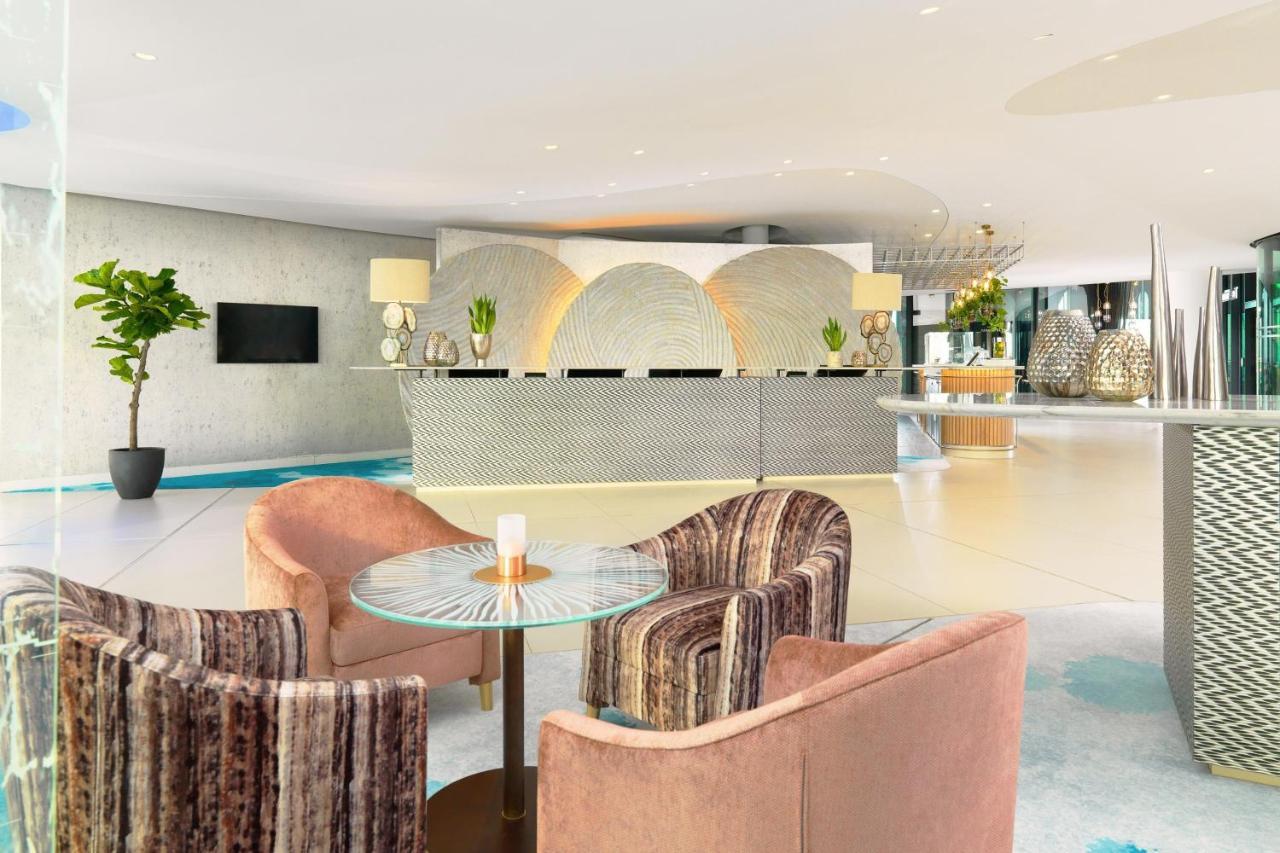 מלון The Westin Hamburg Elbphilharmonie מראה חיצוני תמונה The photo shows a modern hotel lobby with a stylish reception area. The reception desk has a sleek, contemporary design and is centered against a light-colored wall featuring abstract patterns. 

In front of the desk, there are two sets of seating ar