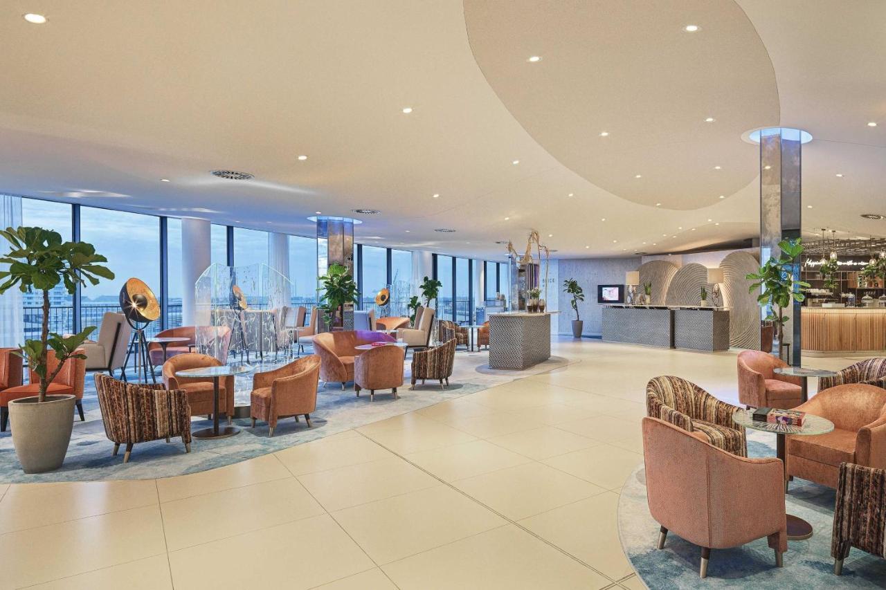 מלון The Westin Hamburg Elbphilharmonie מראה חיצוני תמונה The image shows a modern, stylish interior, likely from a hotel or upscale lounge. The space features large windows that allow natural light to flood in, offering a view of the outside. There's a mix of comfortable seating arrangements, including sev