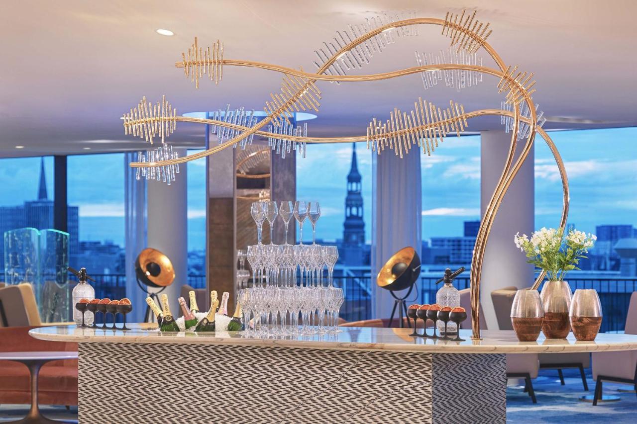 מלון The Westin Hamburg Elbphilharmonie מראה חיצוני תמונה The photo depicts a stylish bar setup in a modern venue. The bar features an elegant design with a patterned front and a sleek countertop. Above the bar, there is a striking decorative element that resembles a stylized tree or wave, made from metalli