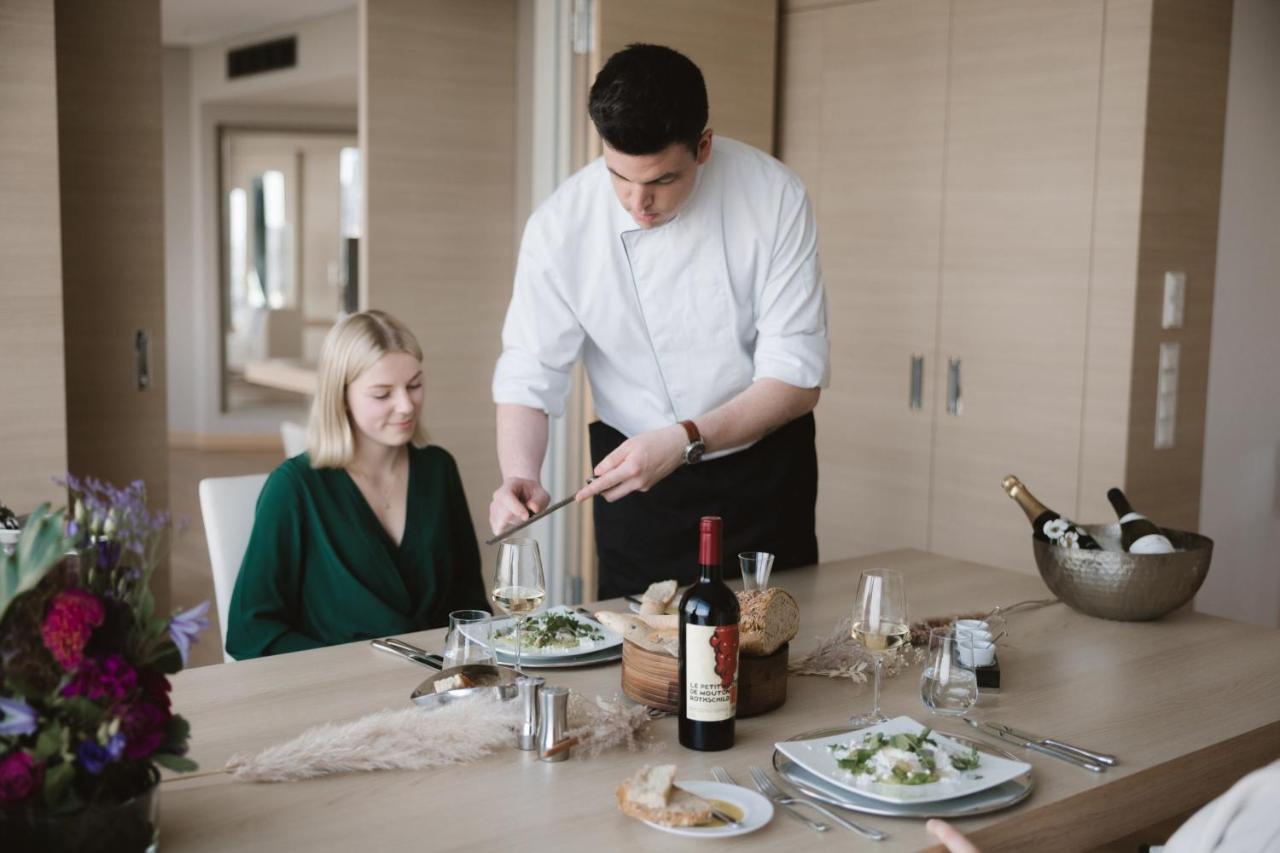 מלון The Westin Hamburg Elbphilharmonie מראה חיצוני תמונה The photo depicts a dining scene in a modern setting. A man, dressed in a chef's attire, is serving food to a woman seated at the table. The woman is wearing a green outfit and appears to be enjoying the meal. The table is elegantly set with plates o