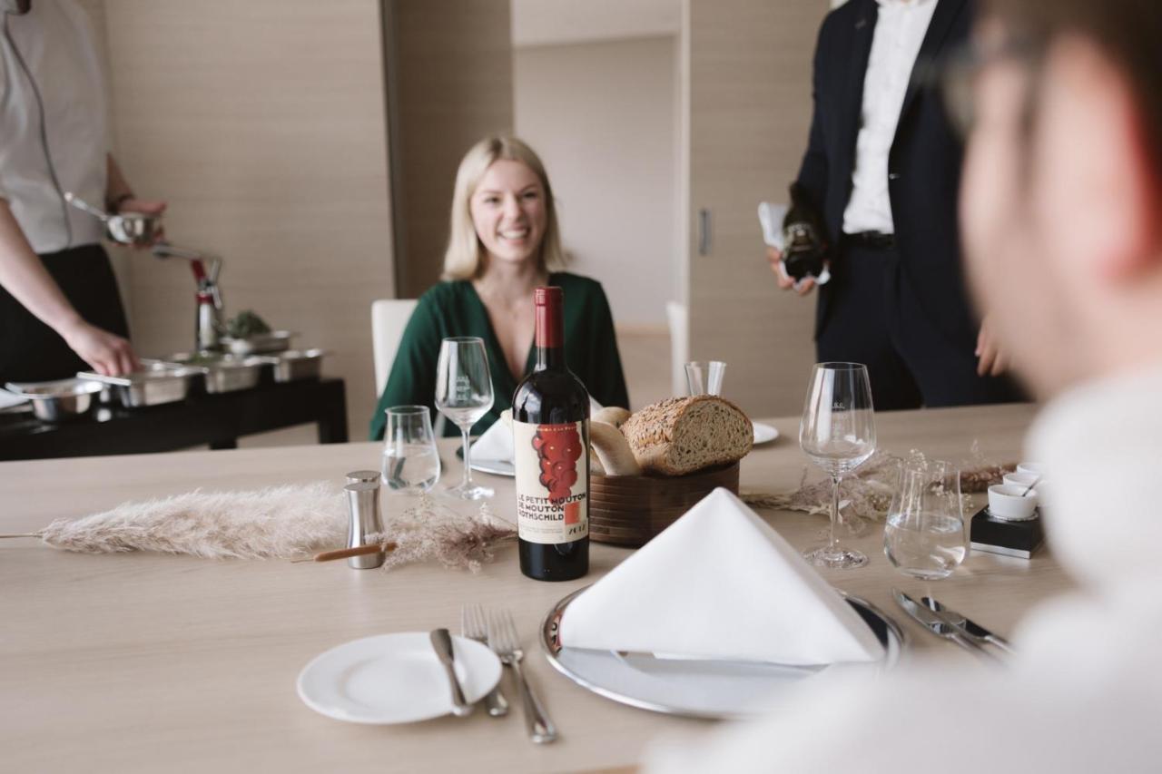 מלון The Westin Hamburg Elbphilharmonie מראה חיצוני תמונה The image shows a dining setting with a woman smiling at the table. She is seated in front of a bottle of red wine that has a distinctive label. There is also bread and a neatly arranged table setting, including plates and glasses. In the background,