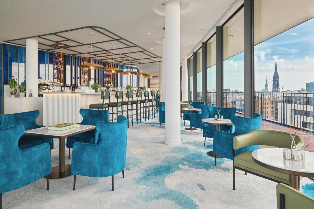 מלון The Westin Hamburg Elbphilharmonie מראה חיצוני תמונה The image shows a stylish and modern restaurant interior. There are several tables with blue and green chairs, creating a cozy atmosphere. The flooring features a light carpet with abstract patterns. Large windows provide plenty of natural light and 