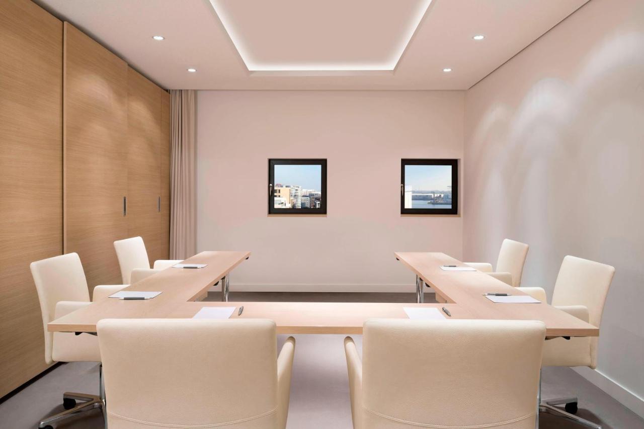 מלון The Westin Hamburg Elbphilharmonie מראה חיצוני תמונה The photo shows a modern conference room. It features a long, rectangular table made of light-colored wood, surrounded by several cream-colored chairs. The walls are painted in a light shade, and there are two framed windows on one wall that provide 