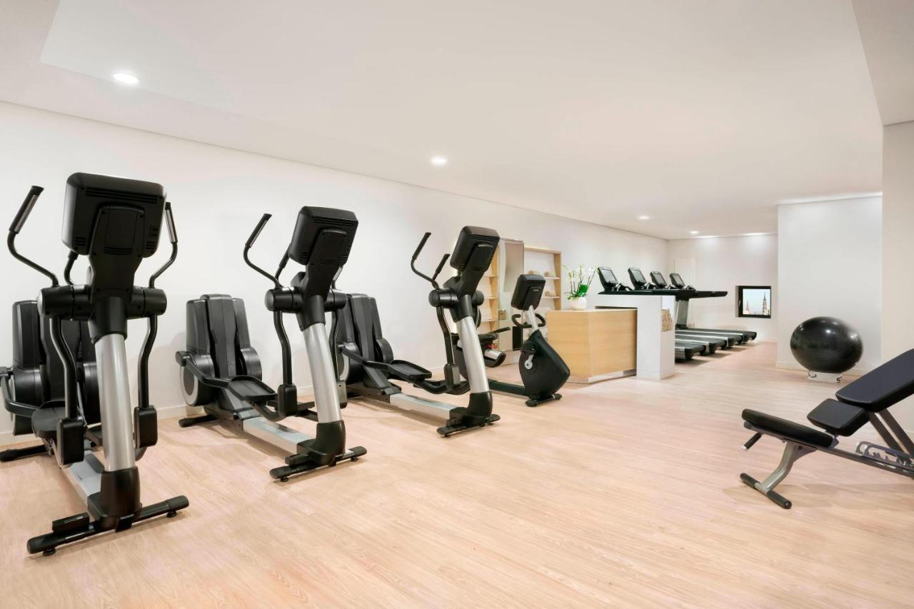מלון The Westin Hamburg Elbphilharmonie מראה חיצוני תמונה The photo shows a fitness room with several pieces of exercise equipment. On the left side, there are multiple elliptical machines arranged in a row. In the center, there is a stationary bike. A workout bench is positioned nearby, and a large exercis