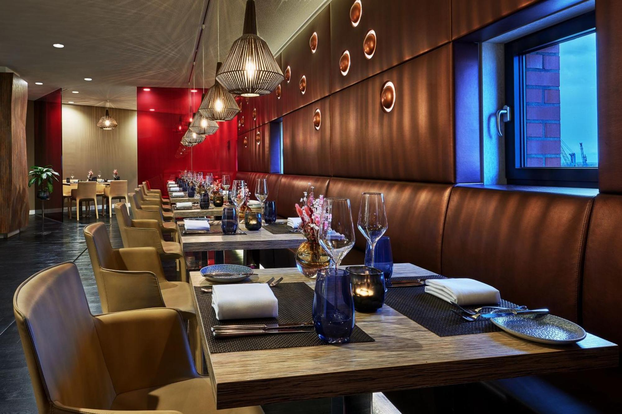 מלון The Westin Hamburg Elbphilharmonie מראה חיצוני תמונה The photo shows a modern restaurant interior. It features a series of wooden tables set for dining, each equipped with white napkins and utensils. The seating consists of comfortable leather chairs. The walls are decorated with a combination of warm 